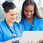 Hospitals Overrun As KILLER Heatwave Continues Two nurses in blue scrubs looking at a tablet