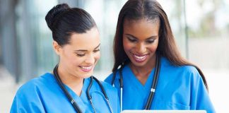 Two nurses in blue scrubs looking at a tablet