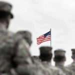 American flag above blurred soldiers in formation