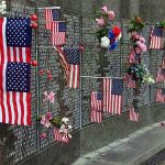 Memorial wall adorned with American flags and flowers