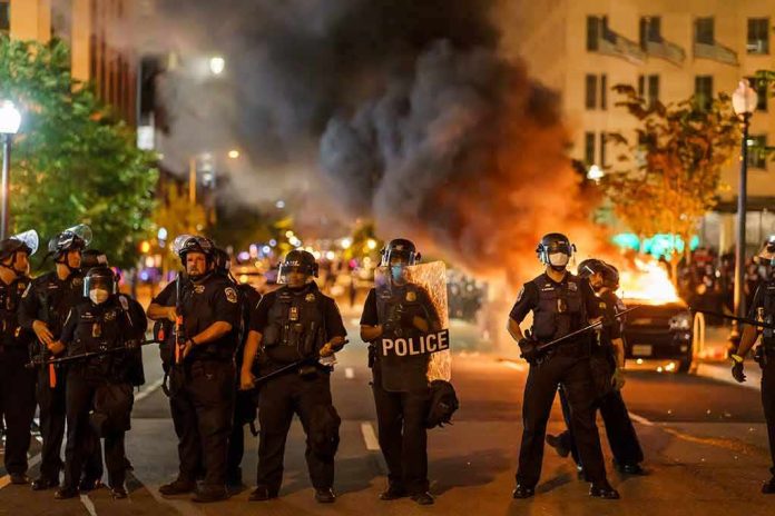 shutterstock_1796220283 Christian Jones and Teddy Williams among police line at night protest with fire and smoke