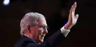 older man in suit raising his hand