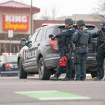 Bizarre Moment Thief Throws Money During Police Chase Police officers gather beside a patrol SUV at a taped-off scene