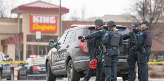 Bizarre Moment Thief Throws Money During Police Chase Police officers gather beside a patrol SUV at a taped-off scene