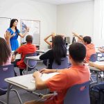 Teacher leading classroom discussion with students raising hands
