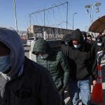 Ebola OUTBREAK – Symptoms You Won’t Believe! People in hoodies and masks walk in a line along a fenced walkway