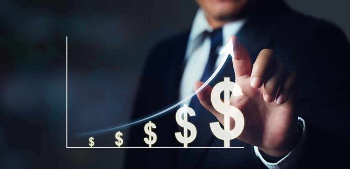 shutterstock_2108280722 Businessperson points to rising dollar symbols on a growth chart