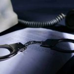 Handcuffs on a document beside a coiled telephone handset