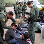 law enforcement officers process a seated group outdoors