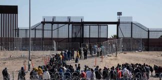 Crowd of people lining up near a border fence with barbed wire