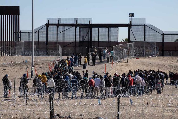 Crowd of people lining up near a border fence with barbed wire
