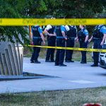Super Drug Hits Streets – Teen Bodies Appear police officers stand behind caution tape at a park scene