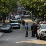Police officers secure a residential street with patrol cars and yellow tape
