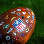 Football with NFL shield and team logos on turf