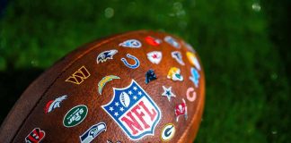 Football with NFL shield and team logos on turf