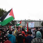 Anti-Jewish Mobs UNLEASH Havoc in NYC Crowd holding flags and signs outside a fenced government building