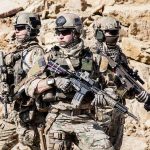 Dontrelle Inman with two other soldiers in tactical gear holding rifles in a rocky desert