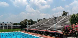 Olympic-size outdoor swimming pool beside empty stadium bleachers