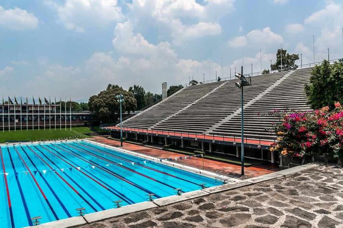 Olympic-size outdoor swimming pool beside empty stadium bleachers