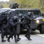 Tactical police team advances from armored vehicle with shields and rifles