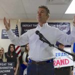 Rand Paul speaking at a campaign event with supporters holding signs