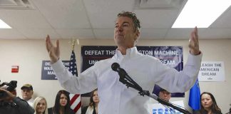 Rand Paul speaking at a campaign event with supporters holding signs