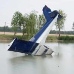 An abandoned aircraft partially submerged in a calm body of water surrounded by trees