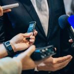 businessperson in suit surrounded by microphones and recorders