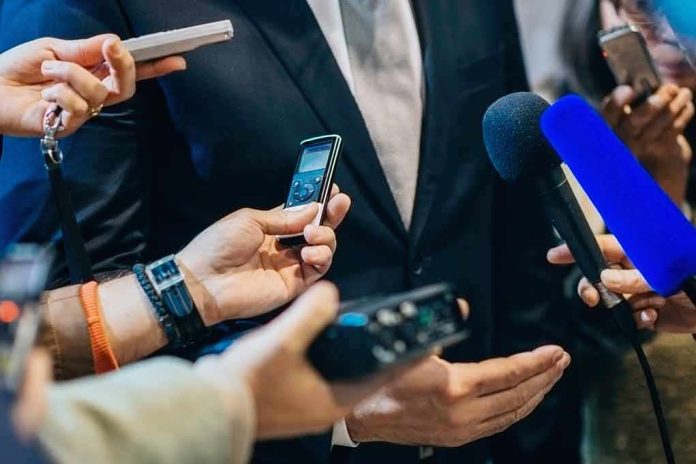 shutterstock_471987556 businessperson in suit surrounded by microphones and recorders