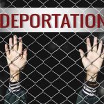Hands gripping chain-link fence with deportation sign