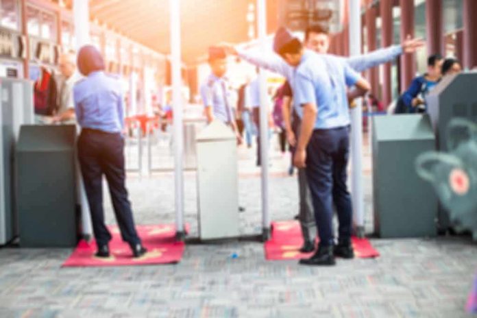 shutterstock_685297528 Security officers screen people at walk-through metal detectors