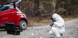 Forensic investigator photographing evidence near a red car on a rural road