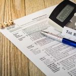 Tax form with calculator and pen on wooden desk