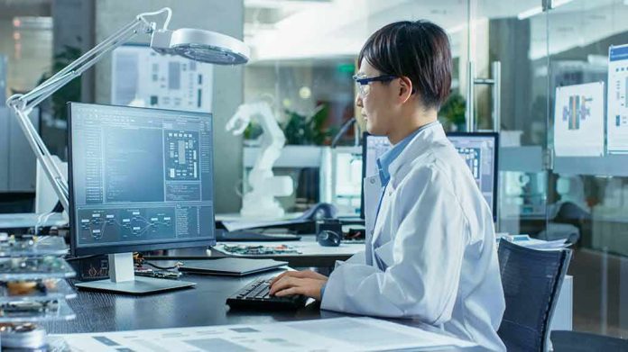 shutterstock_1104131792 Engineer in lab coat working at a computer in a modern lab