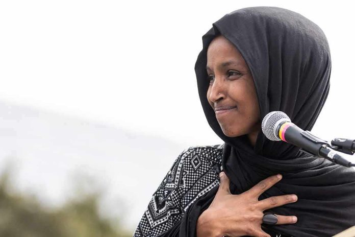 Ilhan Omar speaking at a microphone with hand on chest