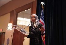 175 House Dems Demand DOJ Drop Criminal Probe of Ilhan Omar Ilhan Omar speaking at a podium with a microphone