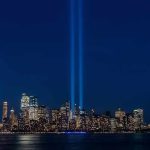 City skyline at night with twin blue light beams rising into the sky