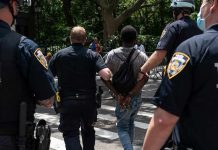 Masked Mob Ambush U.S Journalist – 10 ARRESTED Police escort a handcuffed man across a city street