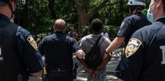 Masked Mob Ambush U.S Journalist – 10 ARRESTED Police escort a handcuffed man across a city street