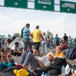 Group of people resting on a roadway beneath highway signs