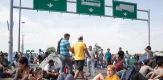 Migrant Caravan Headed North Is Anticipating Democrat Win in Midterms Group of people resting on a roadway beneath highway signs